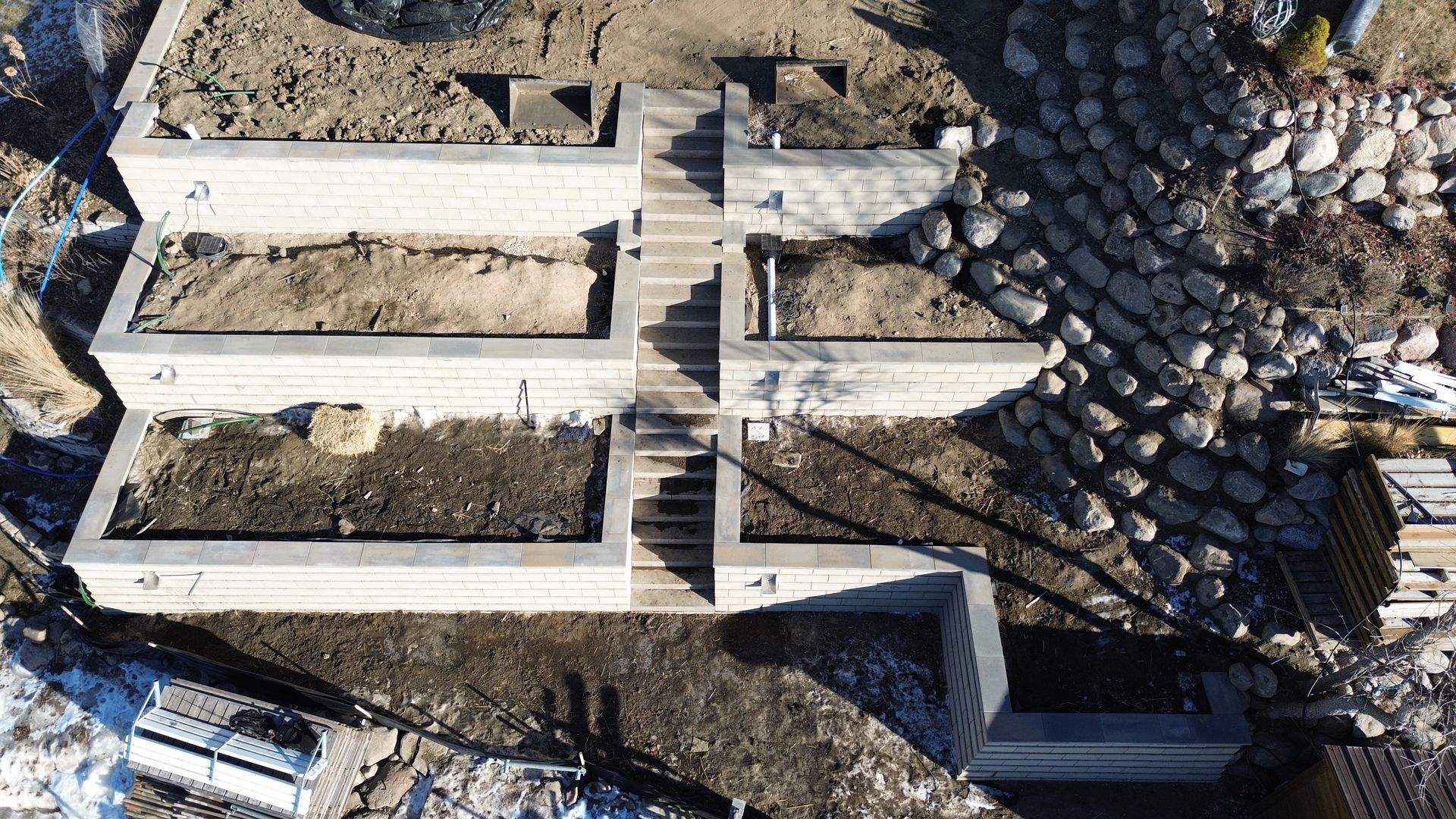 Overhead view of tiered garden beds with stone walls, linked by a central concrete staircase.