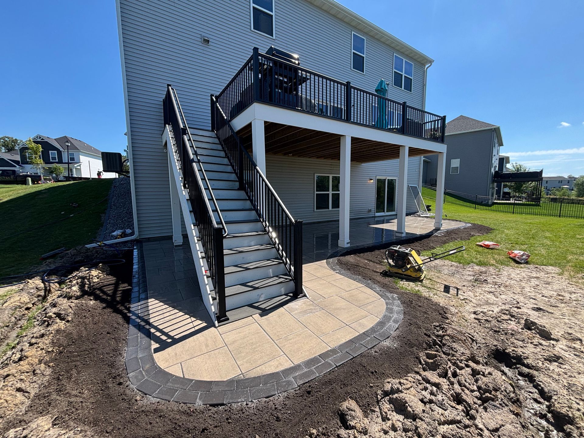 Backyard with a raised deck, stairs, and a newly constructed stone patio.