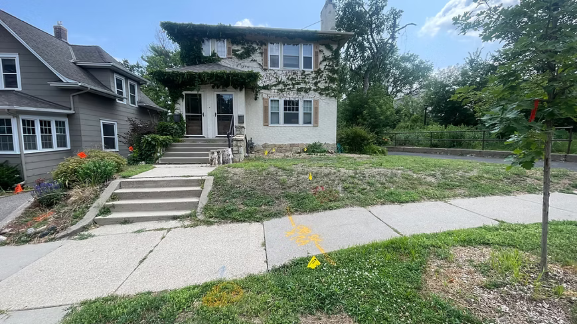 Two-story house with overgrown ivy, a sidewalk, and a grassy yard. Gray house is to the left.