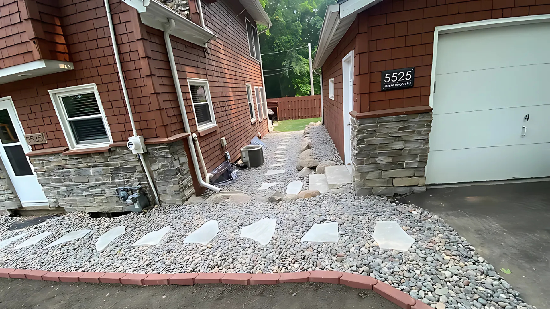 Pathway between two brick buildings with rock beds and stepping stones.