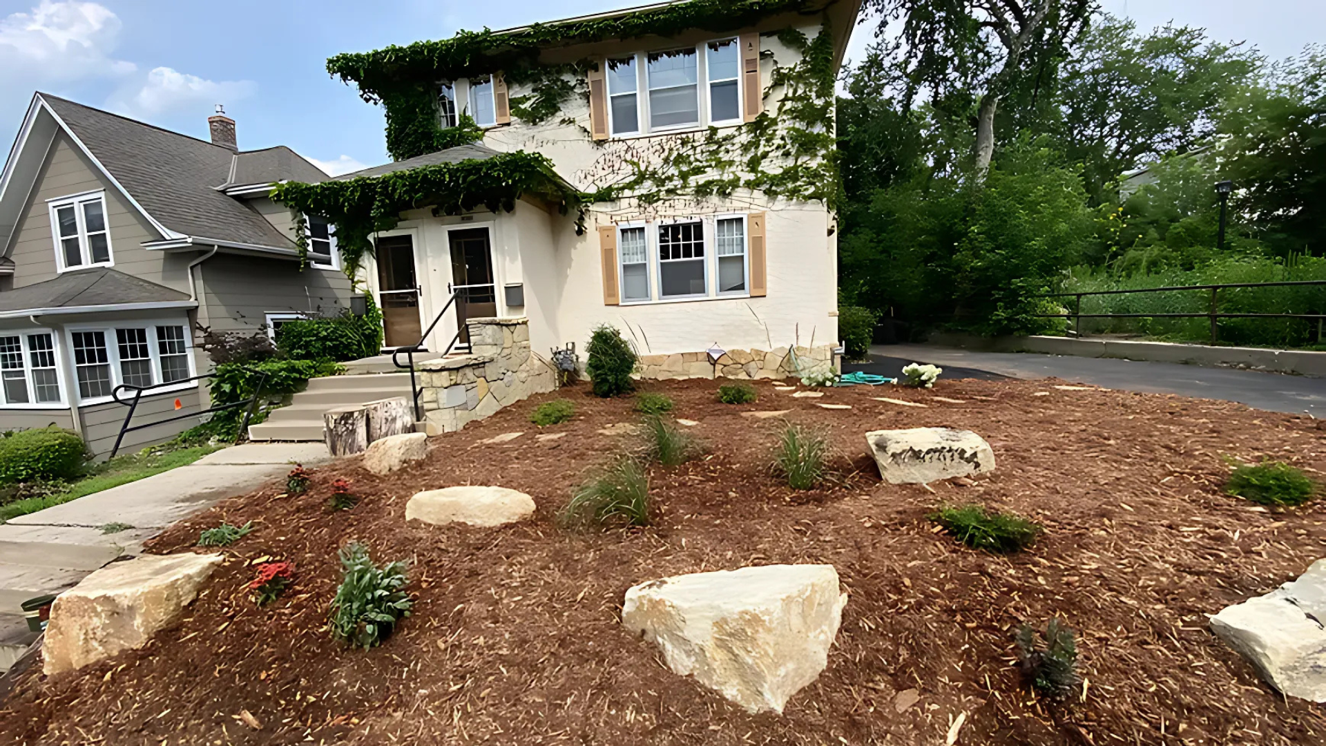 Two-story house with ivy, beige stucco exterior, and landscaped yard with boulders and mulch.