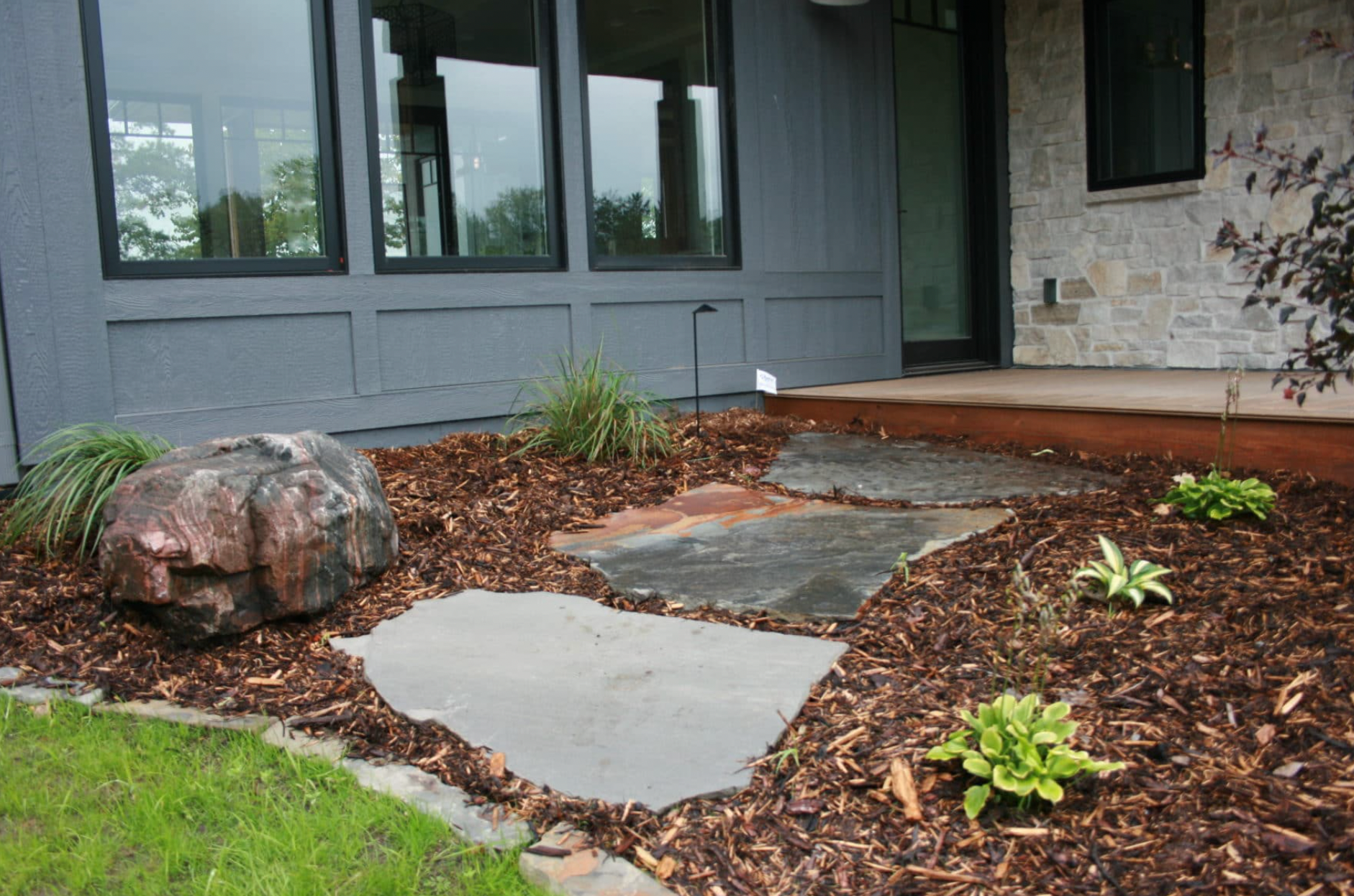 Front yard landscaping with a stone path, mulch, and greenery next to a modern gray house.