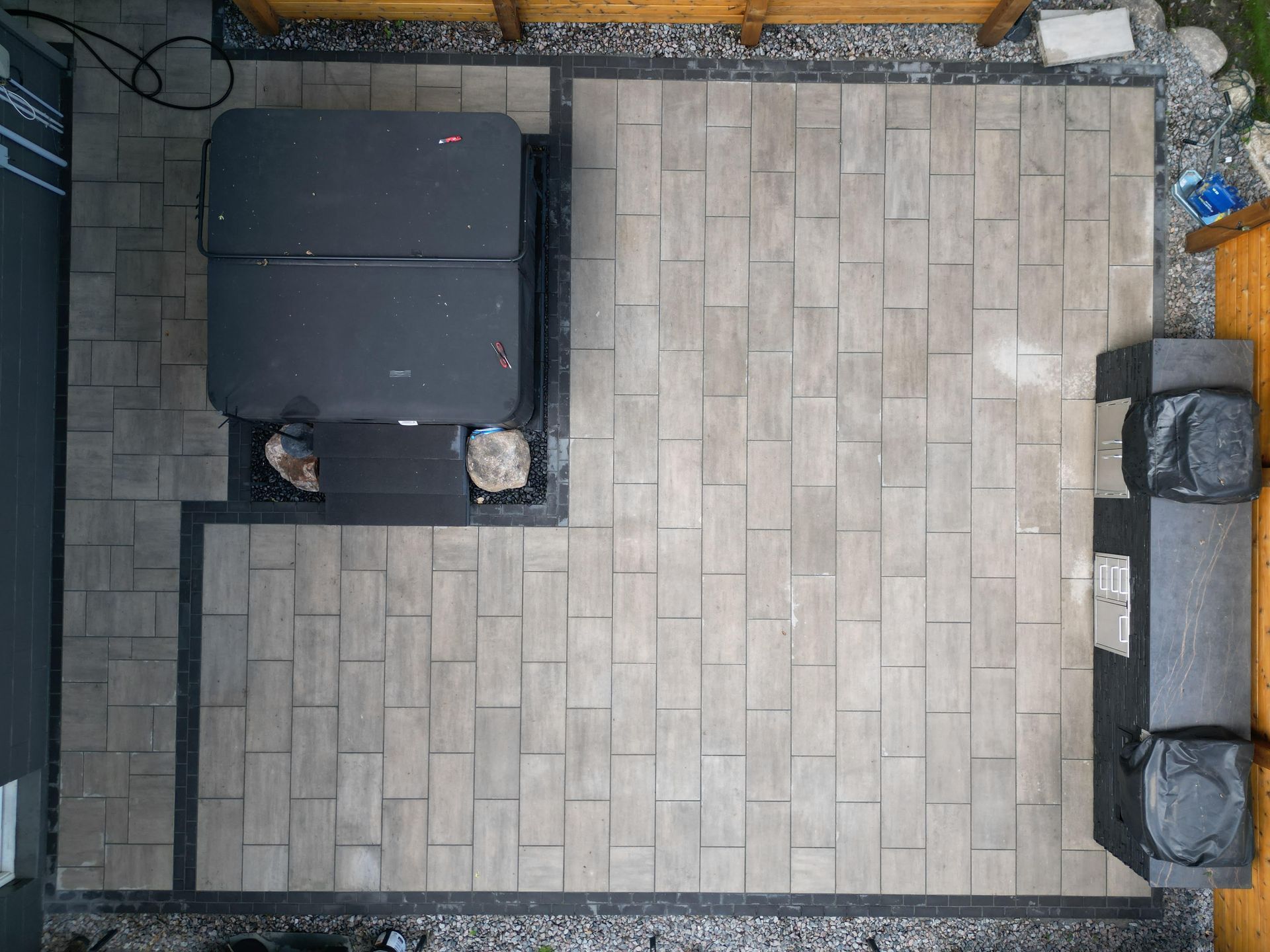 Overhead view of a hot tub and outdoor patio with gray pavers and black borders, next to a wooden fence.