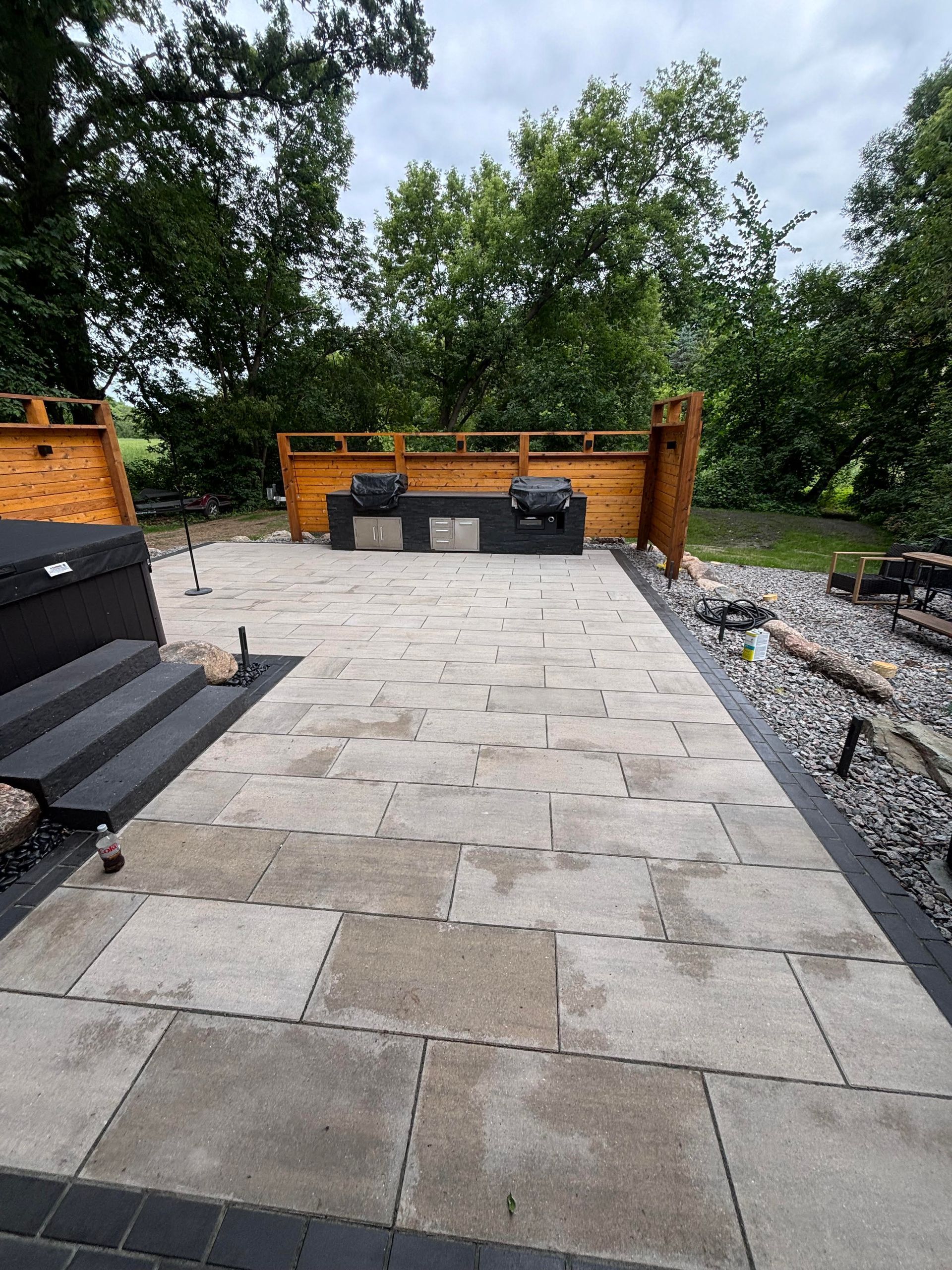 Patio with stone pavers, built-in grill area, steps, and surrounding greenery.