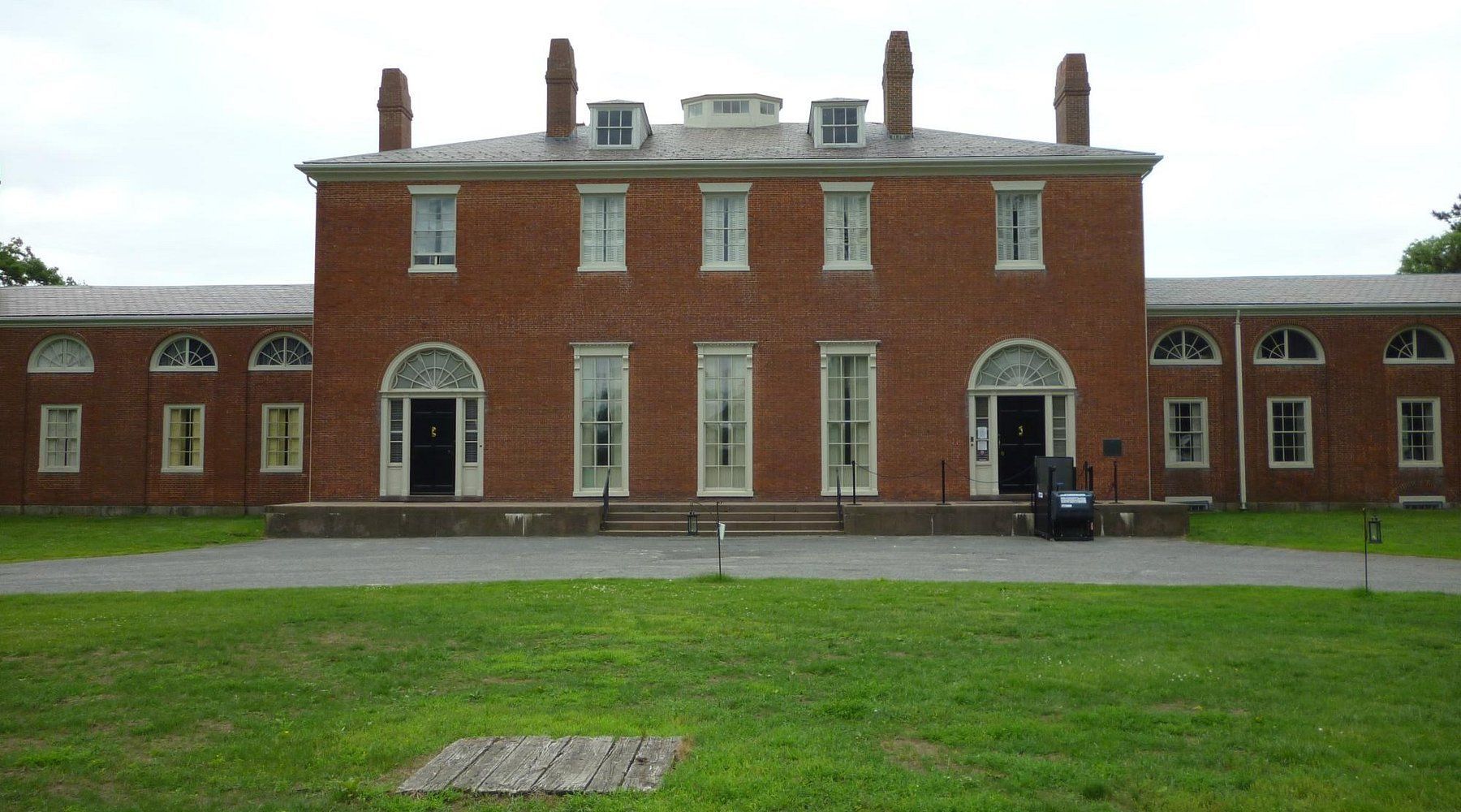 A large brick building with arched windows sits in a grassy field
