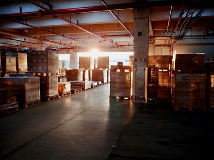 Warehouse interior with packed pallets, sunlight shining through a doorway.