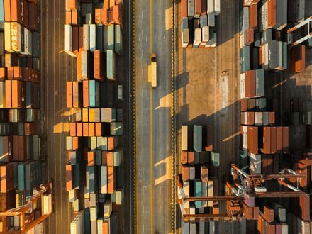 Overhead view of a shipping port with rows of cargo containers and a truck driving down the center road.
