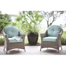 Two wicker chairs with blue cushions are sitting on a patio next to a potted plant.