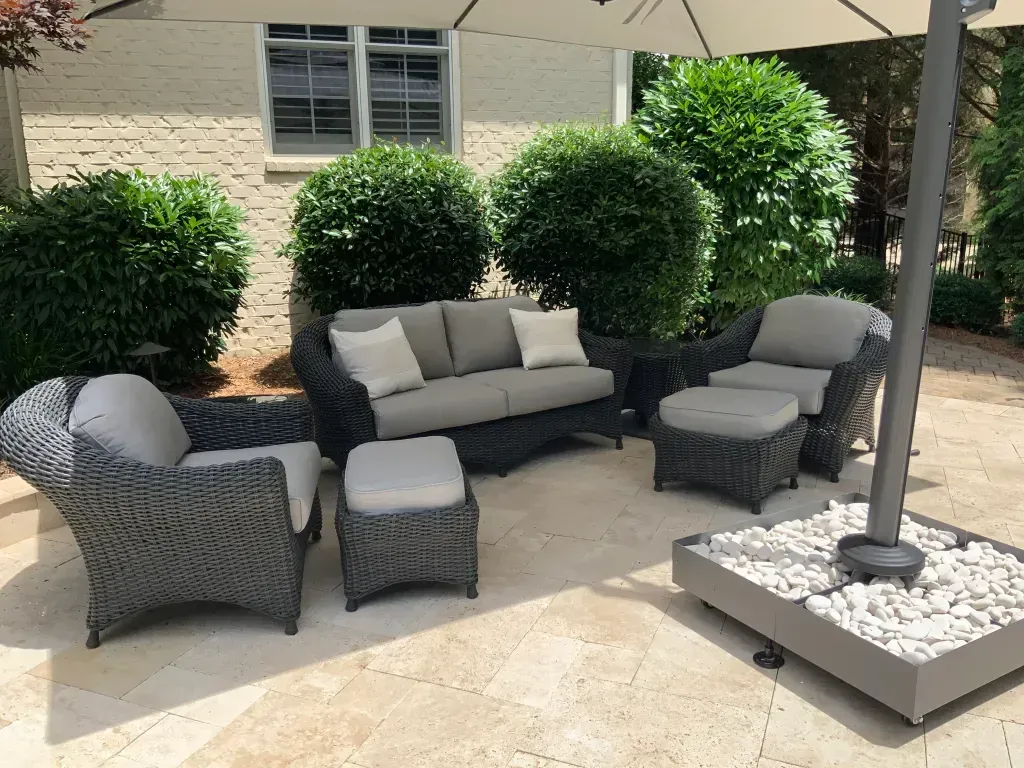 A patio with a couch , chairs , ottoman and umbrella.