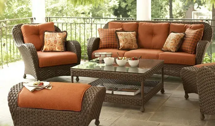 A wicker patio set with orange cushions and pillows