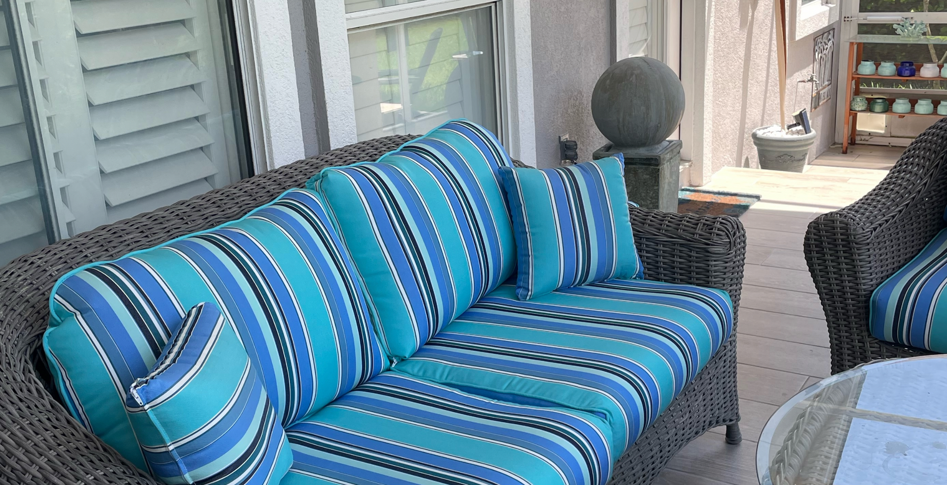 A couch with blue and white stripes on it is on a porch.