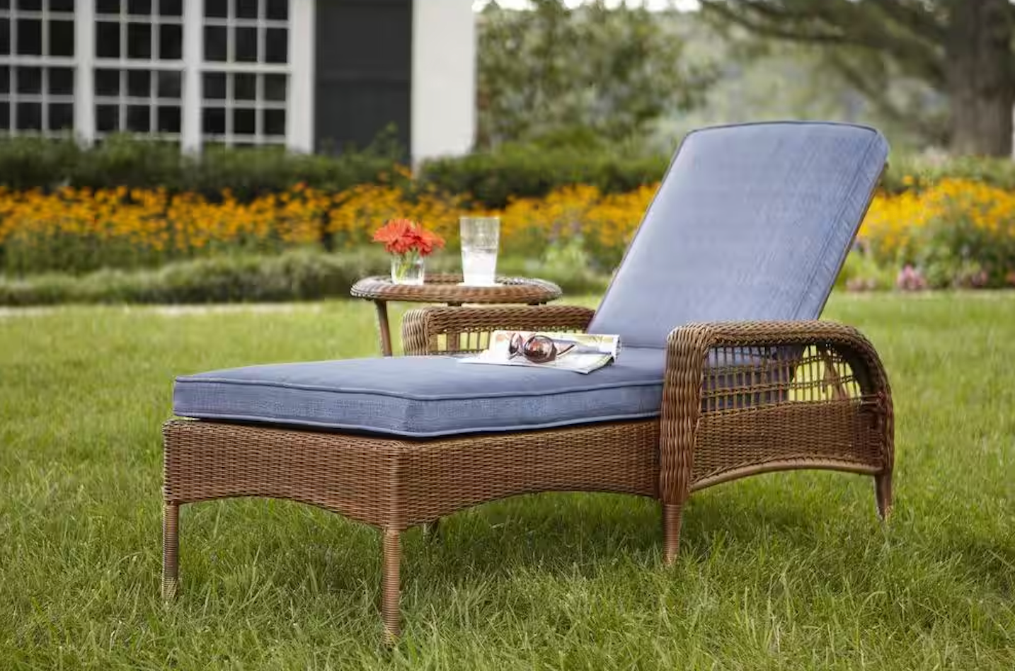 A wicker lounge chair with a blue cushion is sitting in the grass.