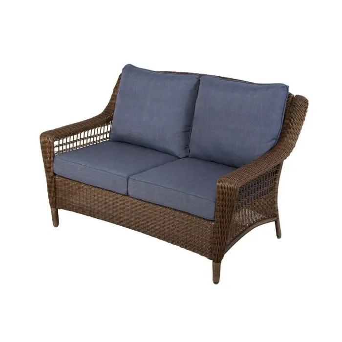A brown wicker outdoor loveseat from the Spring Haven Collection with custom blue outdoor cushions all on a white background.