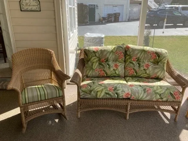 A wicker couch and chair are sitting on a porch next to a window.