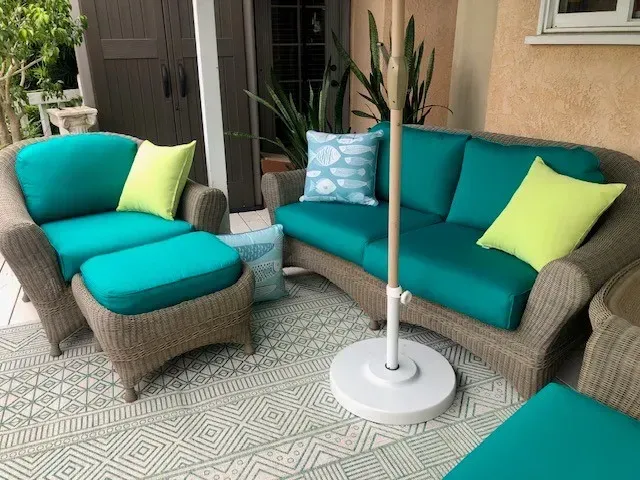 A patio with a couch , chair , ottoman and umbrella