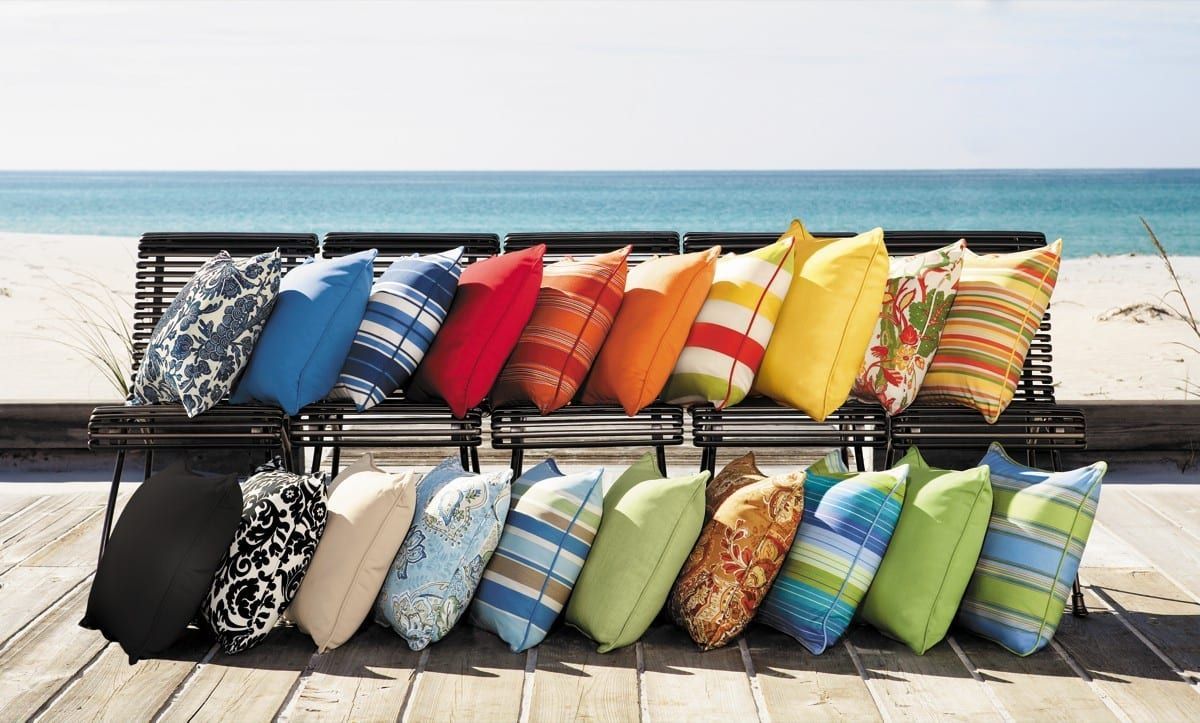 A row of colorful pillows are lined up on a bench near the ocean