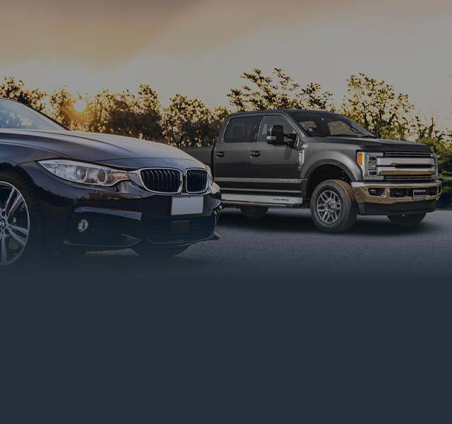 Black car and Black truck parked outside with tree and sun in background | Tveten's Auto Clinic