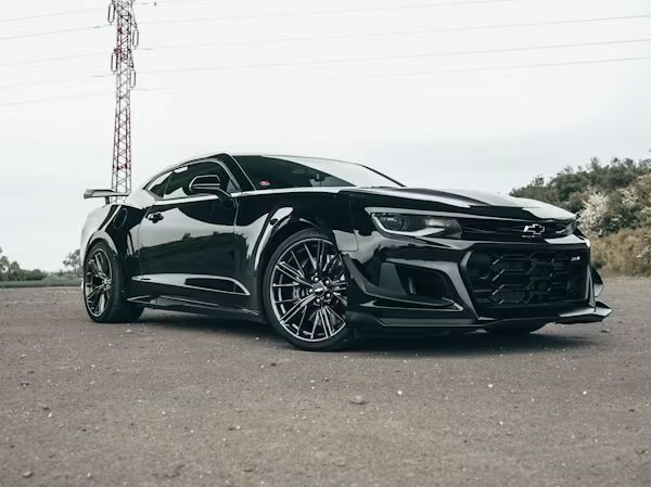 Black sports car parked on a roadside with a cloudy sky and communication tower in the background