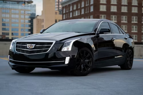 Black Cadillac sedan parked on a rooftop parking area, with city buildings in the background.