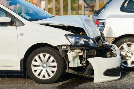 Two cars in a collision; white car with front-end damage, grey car with rear-end damage, outdoors.