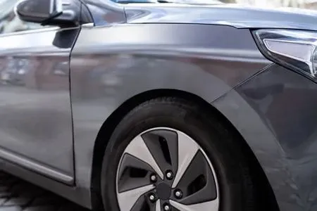 Close-up of a gray sedan’s front side and wheel parked outdoors