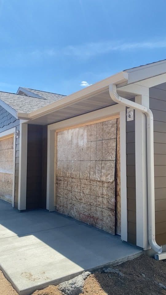 Exterior of a house with a boarded-up garage door and white trim under a clear blue sky