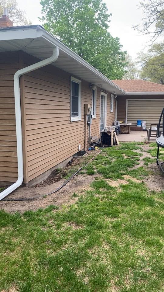 Side of beige house with white trim, small windows, grassy yard, and patio furniture near the back entrance