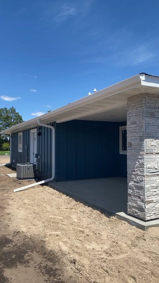 New house exterior with blue walls, stone columns, and a dirt yard under a clear sky