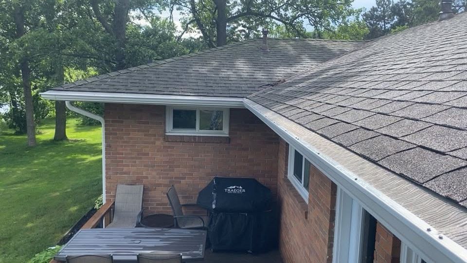Rooftop view of a brick house patio with grill, deck chairs, and green trees in the yard.