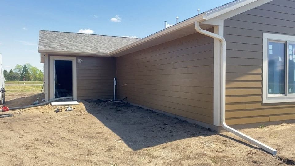 New home exterior with tan siding, white gutters, and a covered entry under construction