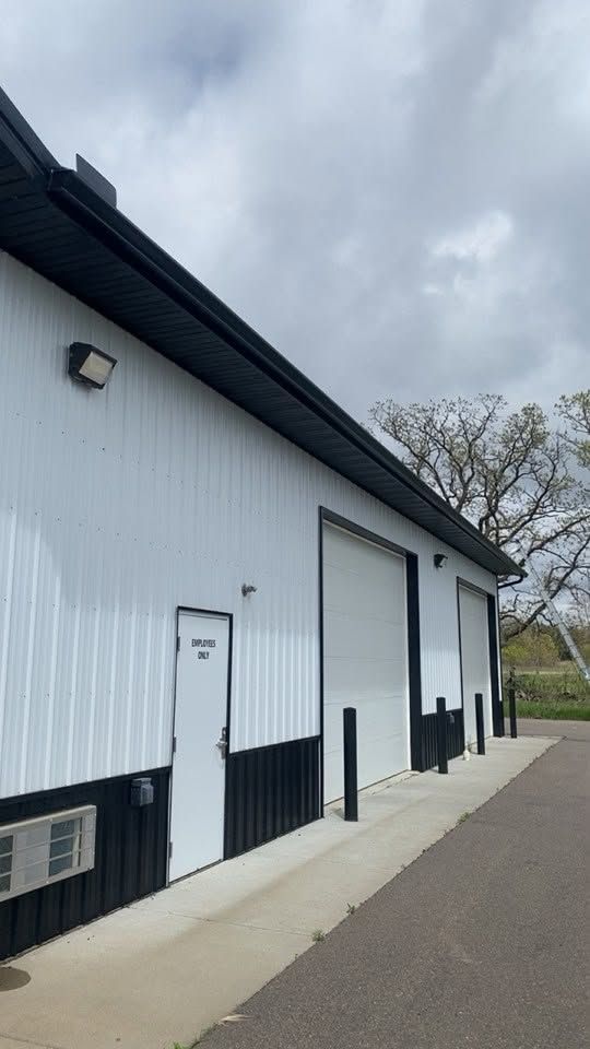 White barn-style building with black trim and a paved walkway under a cloudy sky