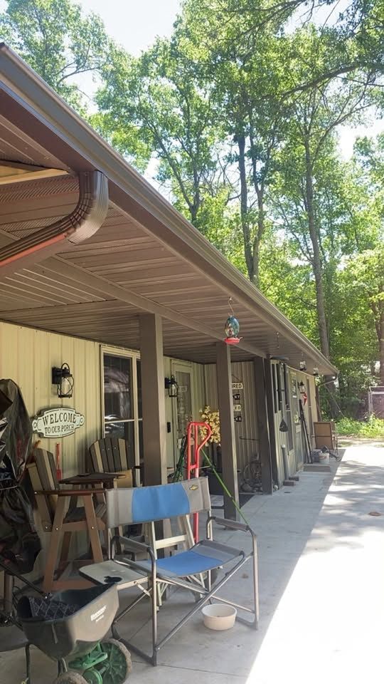 Covered porch with chairs and hanging items beside a wooded driveway