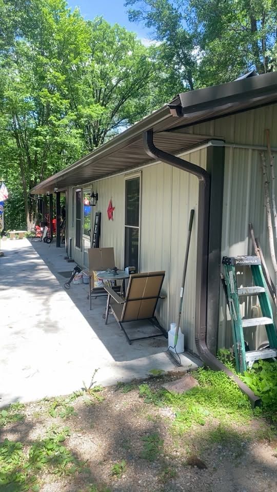 Exterior of a beige building with a covered walkway, patio chairs, and a ladder leaning against the wall.