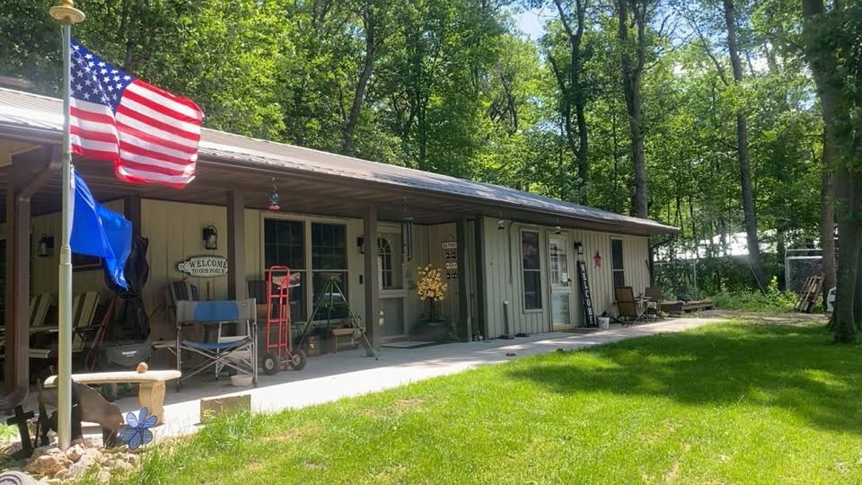 Rustic cabin porch with American flags, surrounded by trees and green lawn