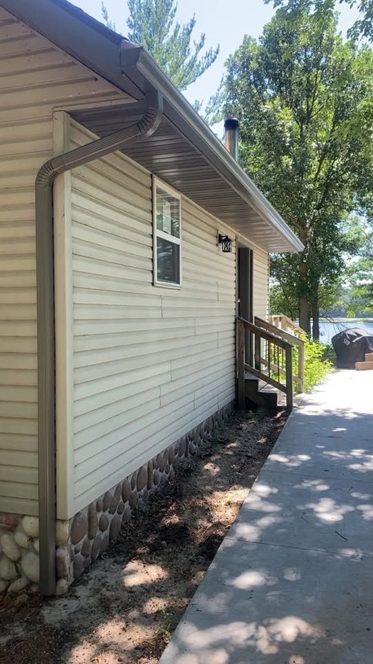 Side view of a beige house with small porch steps beside a paved walkway and trees.