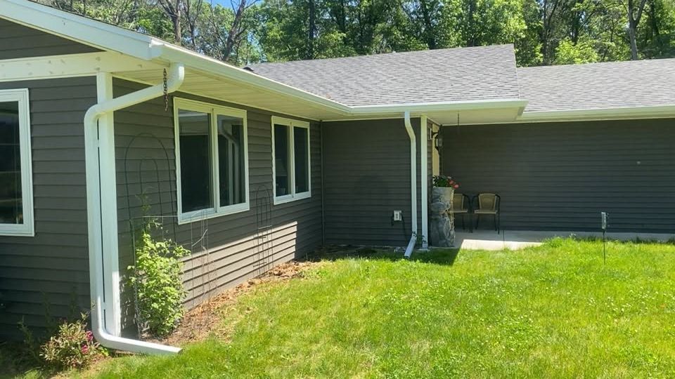 Single-story house with gray siding, white trim, and a bright green lawn in sunlight