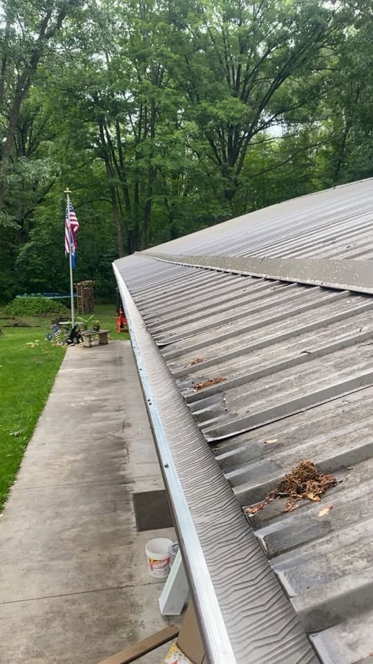 Guttered metal roof beside a concrete driveway and wooded yard with an American flag on a pole.