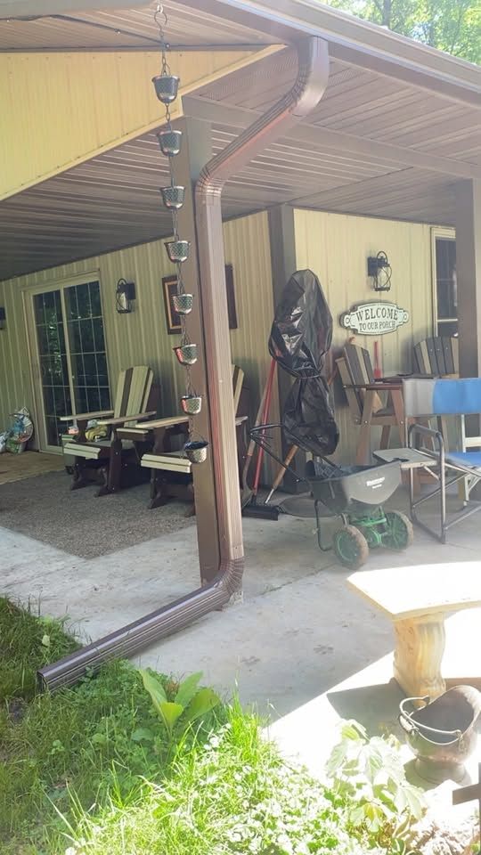 Covered patio with lawn equipment, chairs, and tools beside a house; green yard in foreground