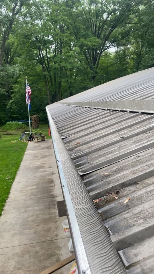 Sloped corrugated roof beside a concrete walkway, with a flagpole and wooded yard in the background
