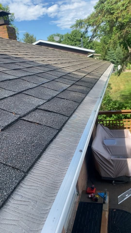 Roof shingles and gutter edge overlooking a covered patio with storage items below.