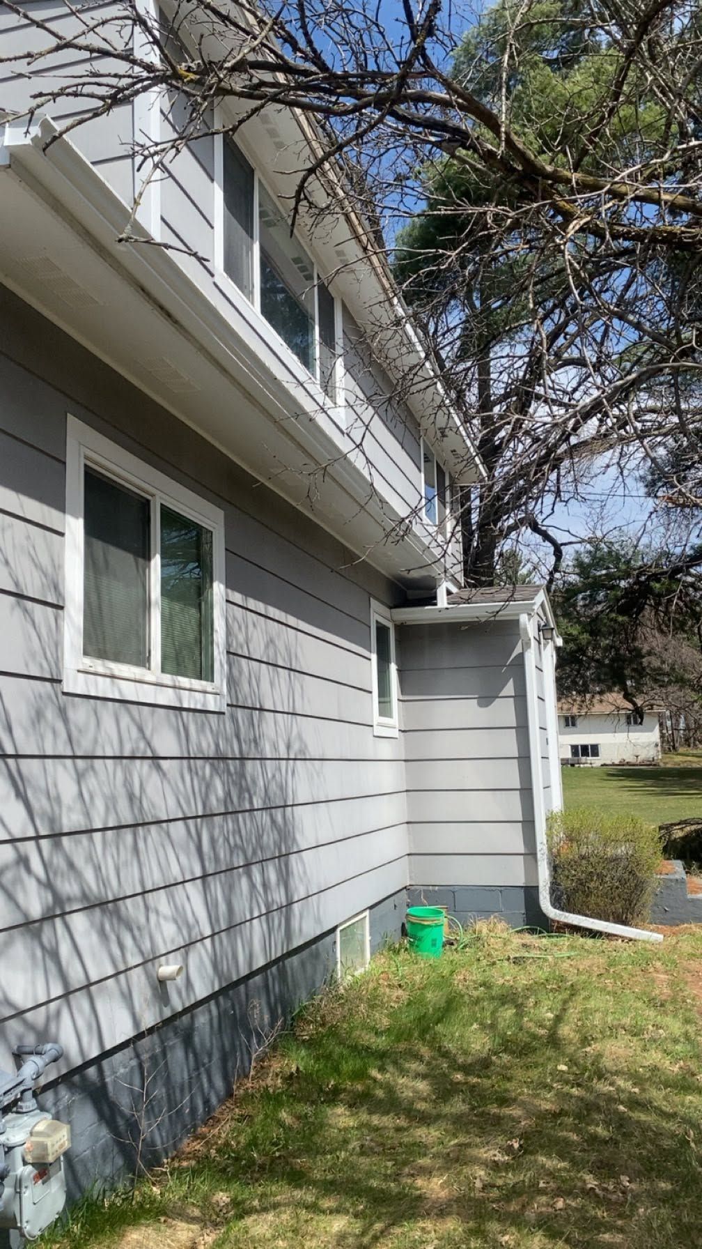 Side of a gray house with white trim, green window, and a tree overhanging a grassy yard.