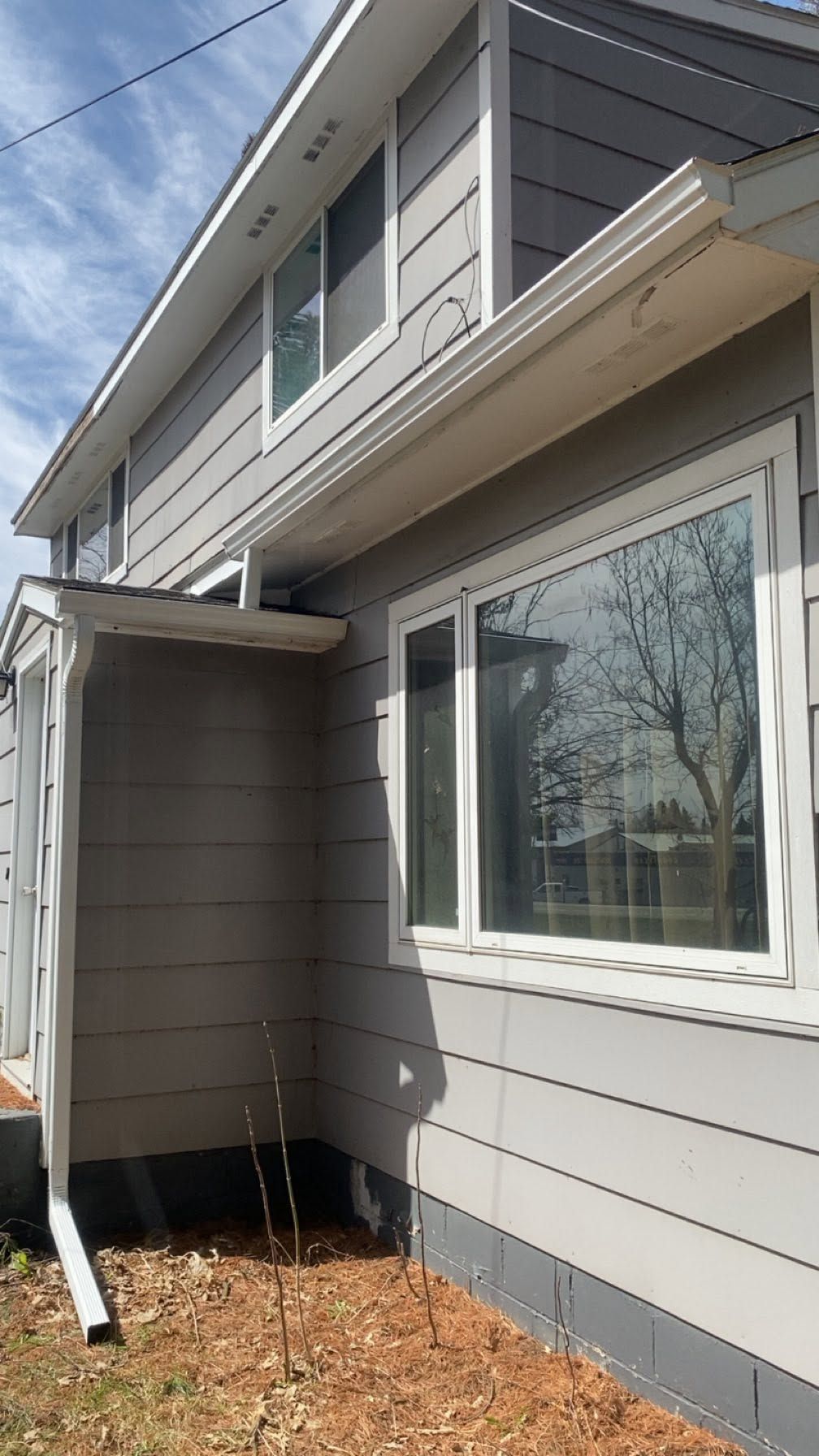 Gray house exterior with a small awning over a side entrance and a large window.