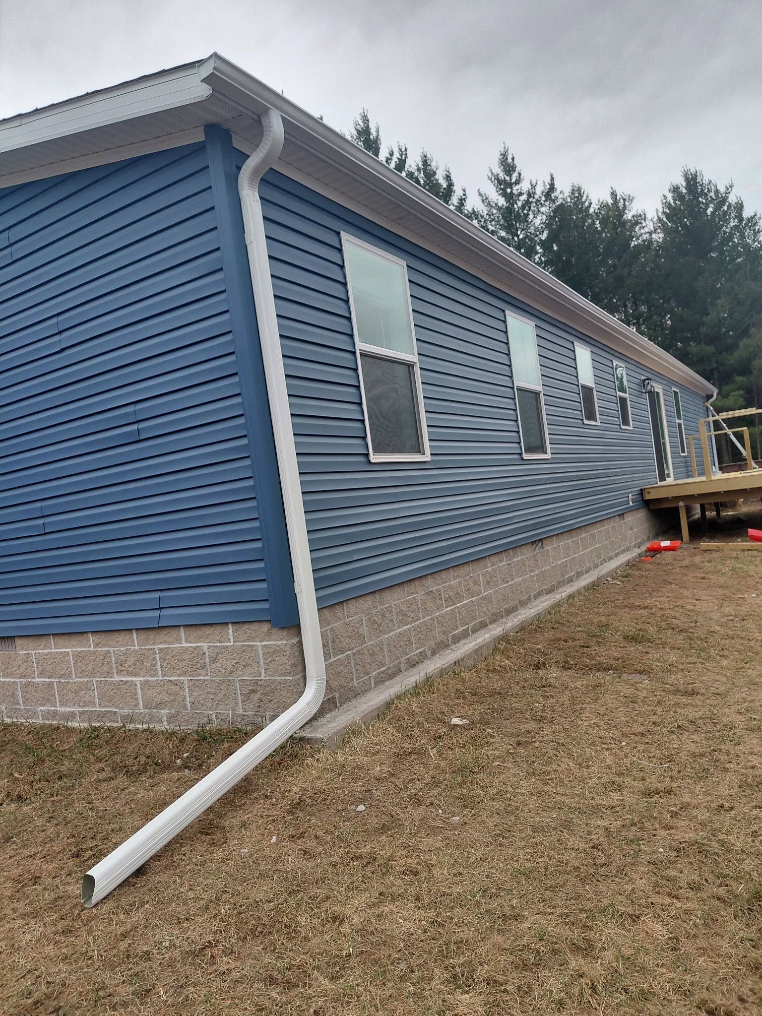 Blue house with white trim and downspout, seen from the side on a gravel yard.