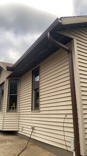 Beige vinyl-sided house exterior with dark roofline and cloudy sky