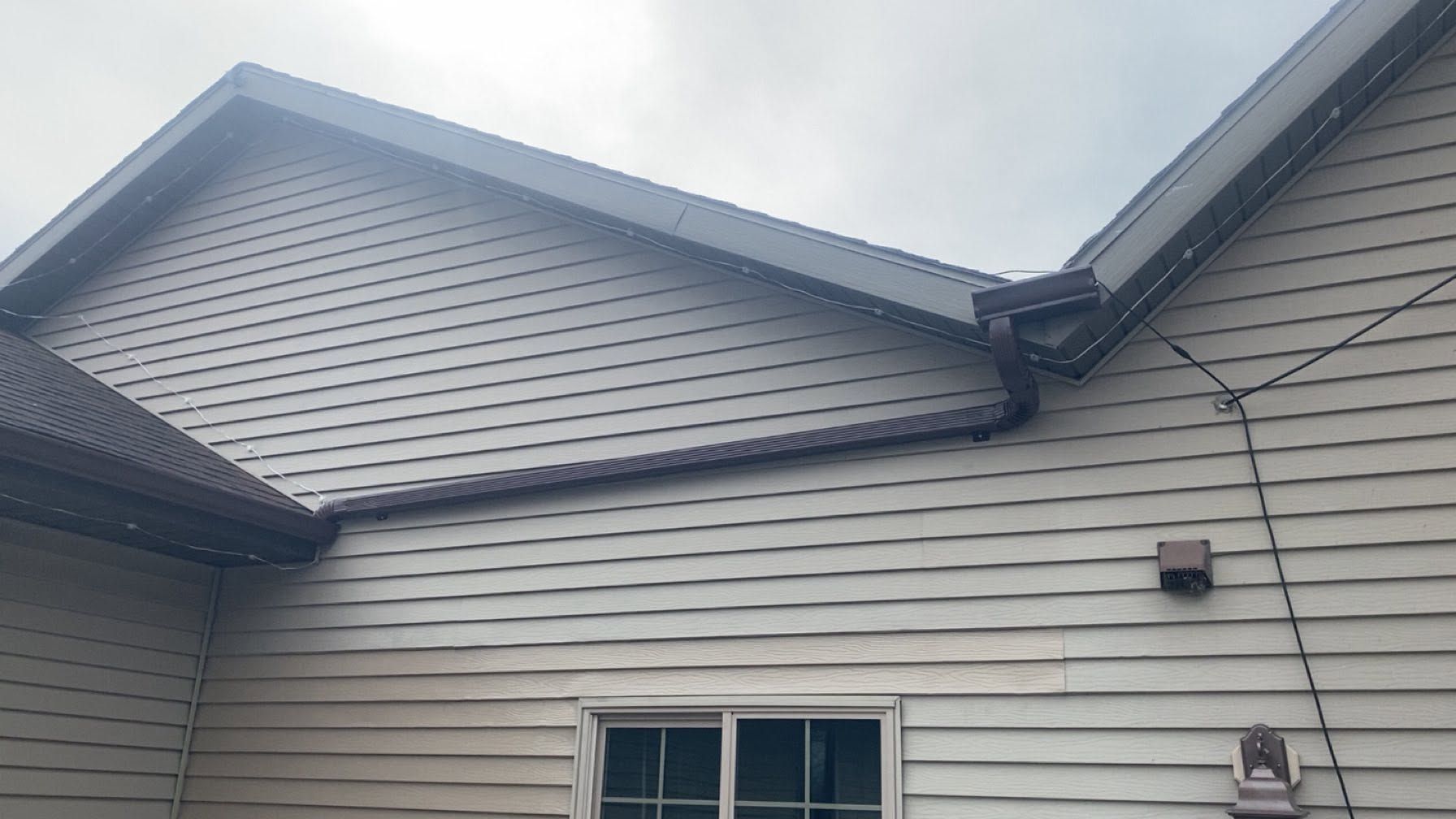 Side view of a beige house with vinyl siding and two roof gables.