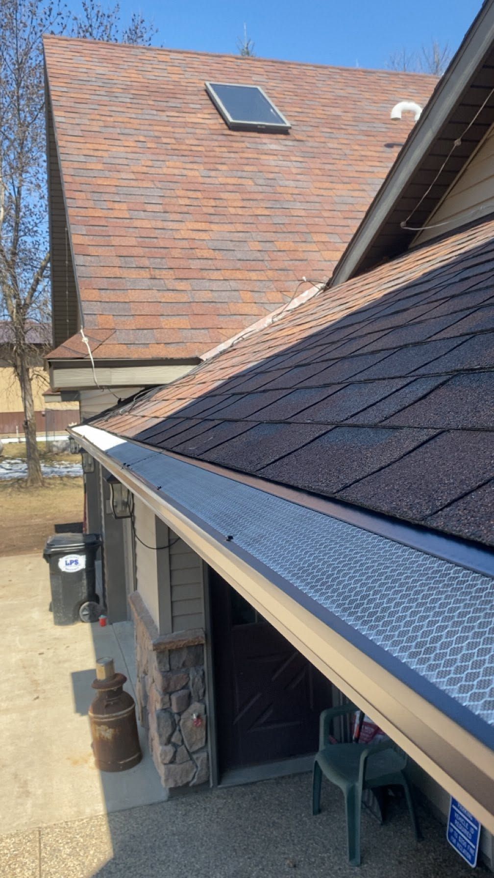 Residential roof with brown shingles, skylight, and gutter above a covered porch.