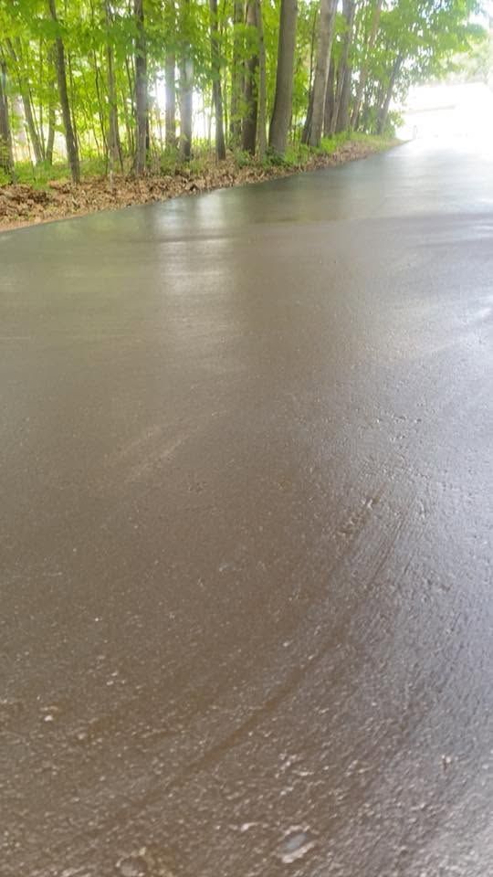 Rainy road beside a green wooded shoreline, with wet pavement reflecting light