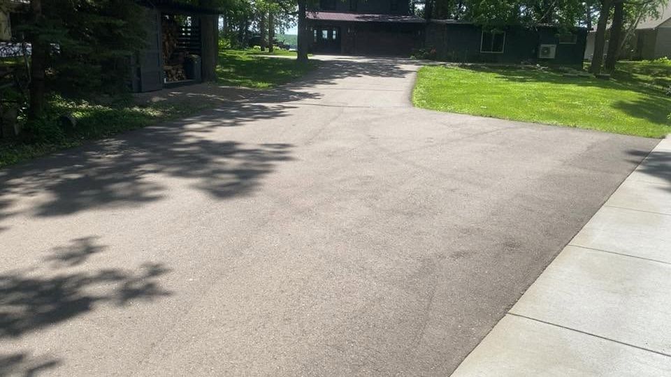 Sunny paved driveway curving past green lawns and trees toward a building entrance
