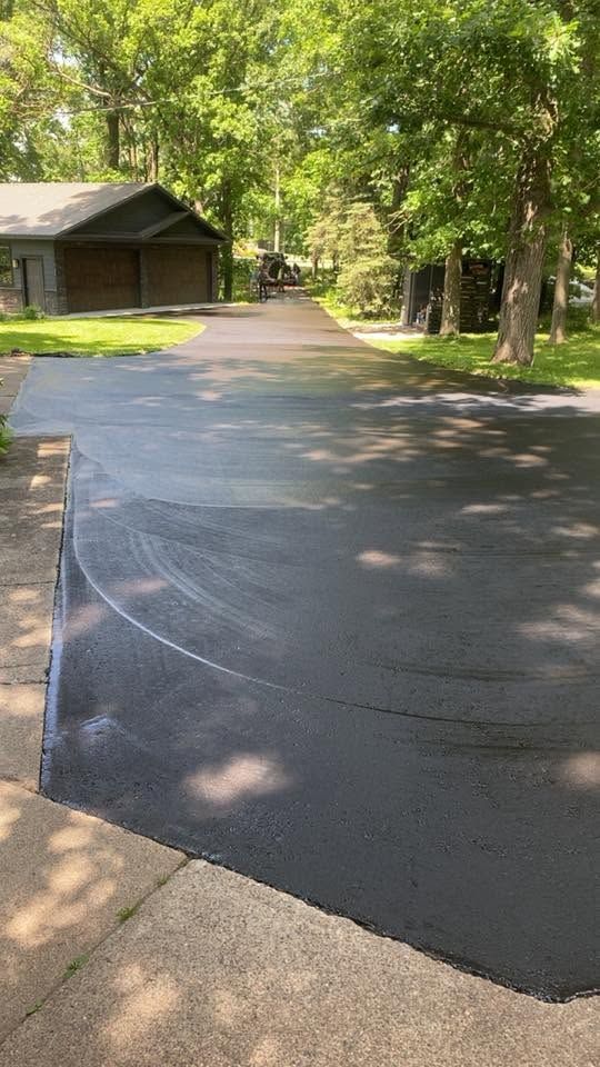Freshly paved driveway leading to a garage beside a tree-lined house on a sunny day