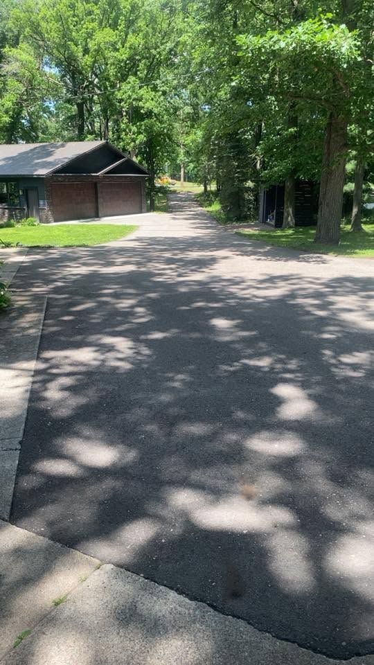 Tree-lined paved path beside a small dark wooden building in a sunny park.